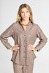 A woman modeling a brown and beige plaid button-up shirt and matching pants set against a light gray studio background.