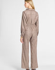 A woman shown from the back wearing a brown and beige plaid pair of pants and top with a high collar, long sleeves, and wide legs, paired with brown shoes, against a light gray studio background.