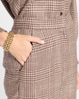 Close-up of a brown and beige plaid pair of pants with a hand tucked into the pocket, wearing a chunky gold chain bracelet.