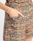 Close-up of a person wearing a multicolor tweed mini skirt with a side pocket and a silver beaded bracelet on the wrist, against a plain light background.