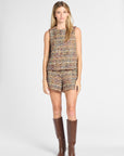 A woman modeling a sleeveless tweed top and matching shorts set in a multicolor woven pattern, paired with brown knee-high boots, against a light gray studio background.