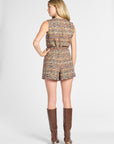 A woman shown from the back wearing a sleeveless tweed romper in a multicolor woven pattern with brown knee-high heeled boots, photographed against a light gray studio background.