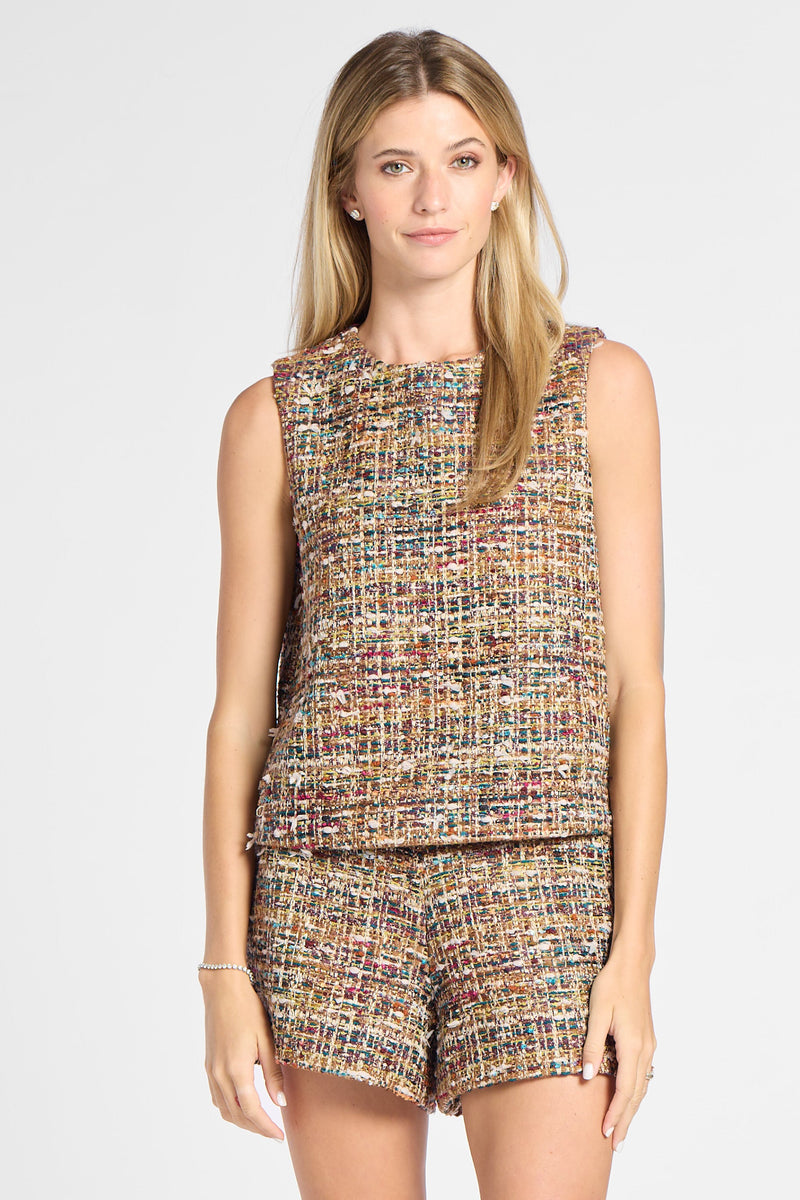 A woman modeling a sleeveless tweed top and matching shorts set in a multicolor woven pattern, paired with brown knee-high boots, against a light gray studio background.