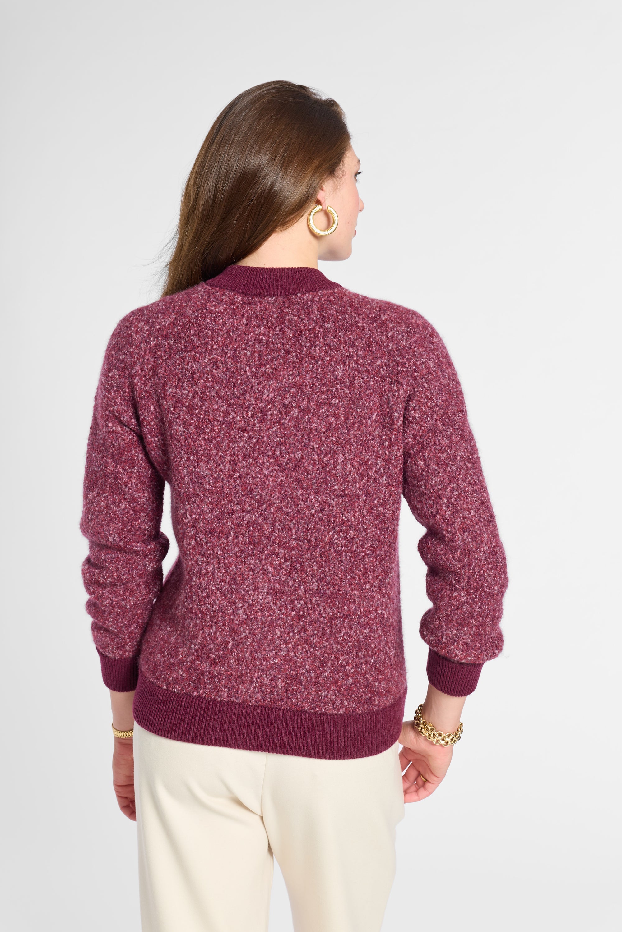 A woman shown from the back wearing a marled burgundy knit sweater and cream pants against a light gray studio background.