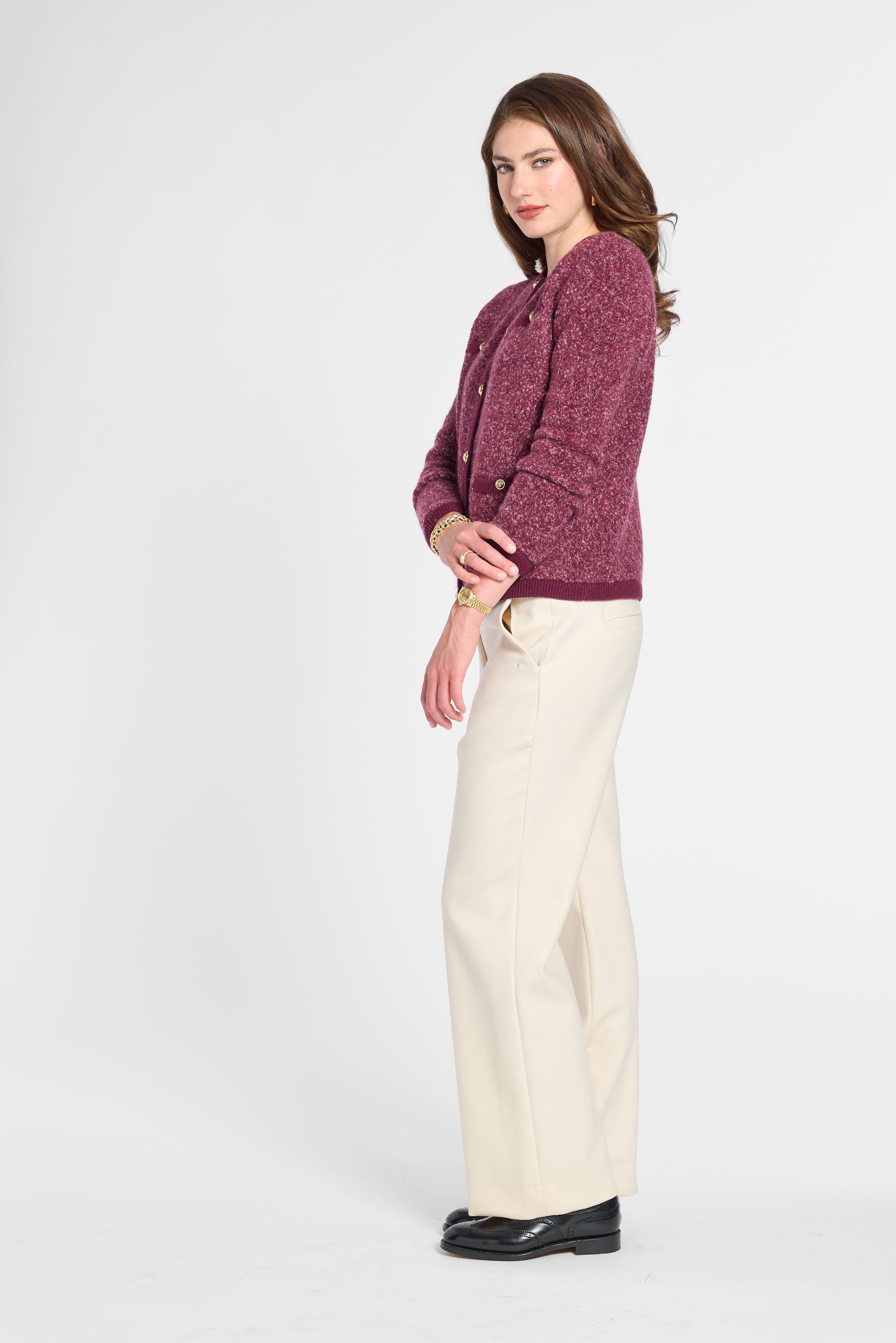 A woman modeling a textured burgundy knit cardigan and cream wide-leg trousers against a light gray studio background.