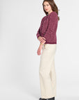 A woman modeling a textured burgundy knit cardigan and cream wide-leg trousers against a light gray studio background.