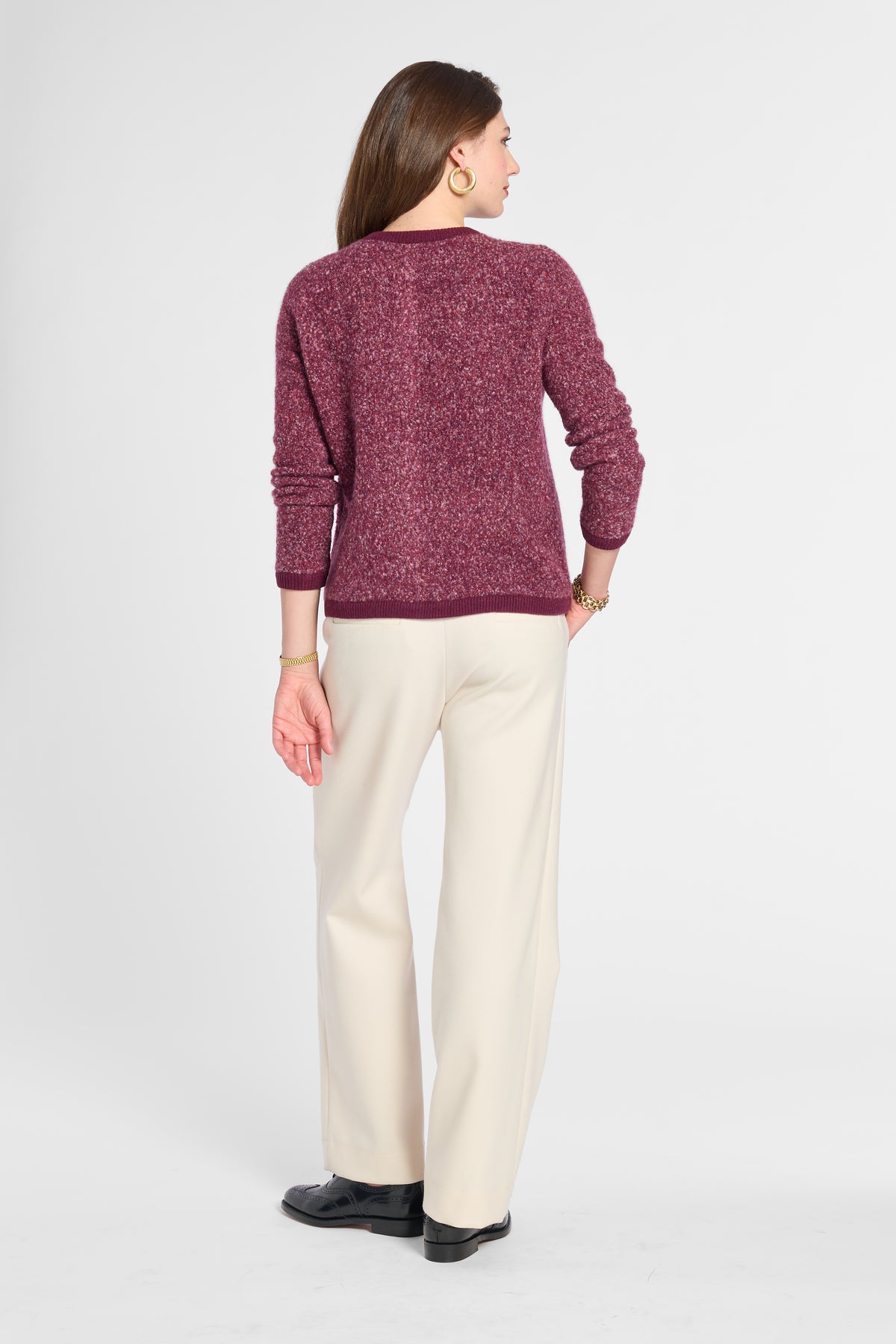 A woman shown from the back wearing a textured marled burgundy sweater and cream wide-leg trousers, standing against a light gray studio background.