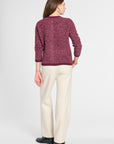 A woman shown from the back wearing a textured marled burgundy sweater and cream wide-leg trousers, standing against a light gray studio background.