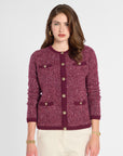 A woman modeling a textured tweed cardigan in burgundy with gold-tone buttons and flap pockets, paired with cream trousers, against a light gray studio background.
