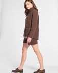 A woman modeling a brown knit cardigan sweater and matching brown mini skirt, paired with brown leather oxford shoes, against a light gray studio background.