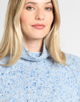 A close-up of a woman wearing a light blue knit turtleneck sweater with subtle blue and white speckles, set against a plain light gray background.