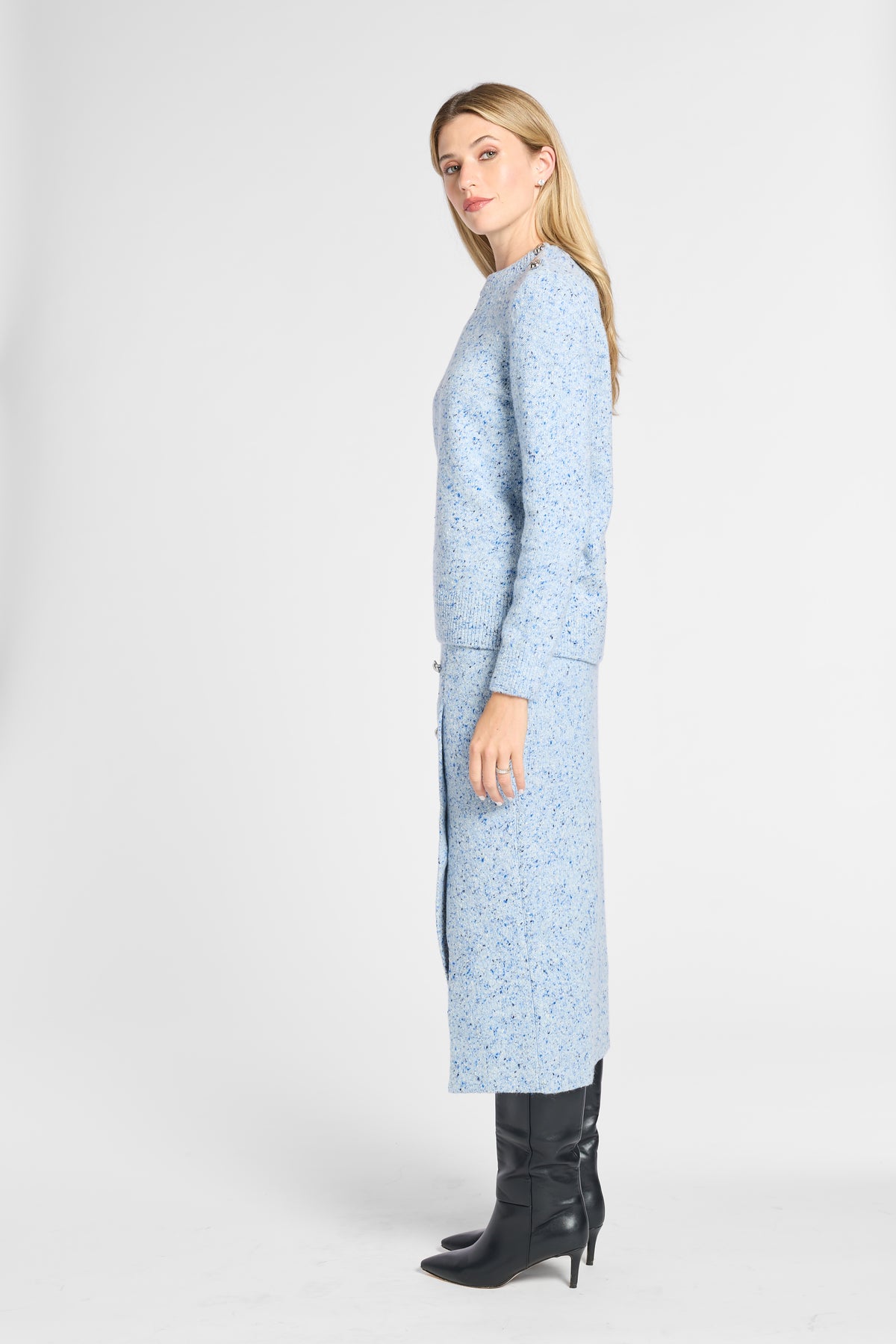 A woman modeling a light blue long-sleeve knit cardigan with a subtle floral pattern, paired with black knee-high boots, photographed against a plain light gray studio background.
