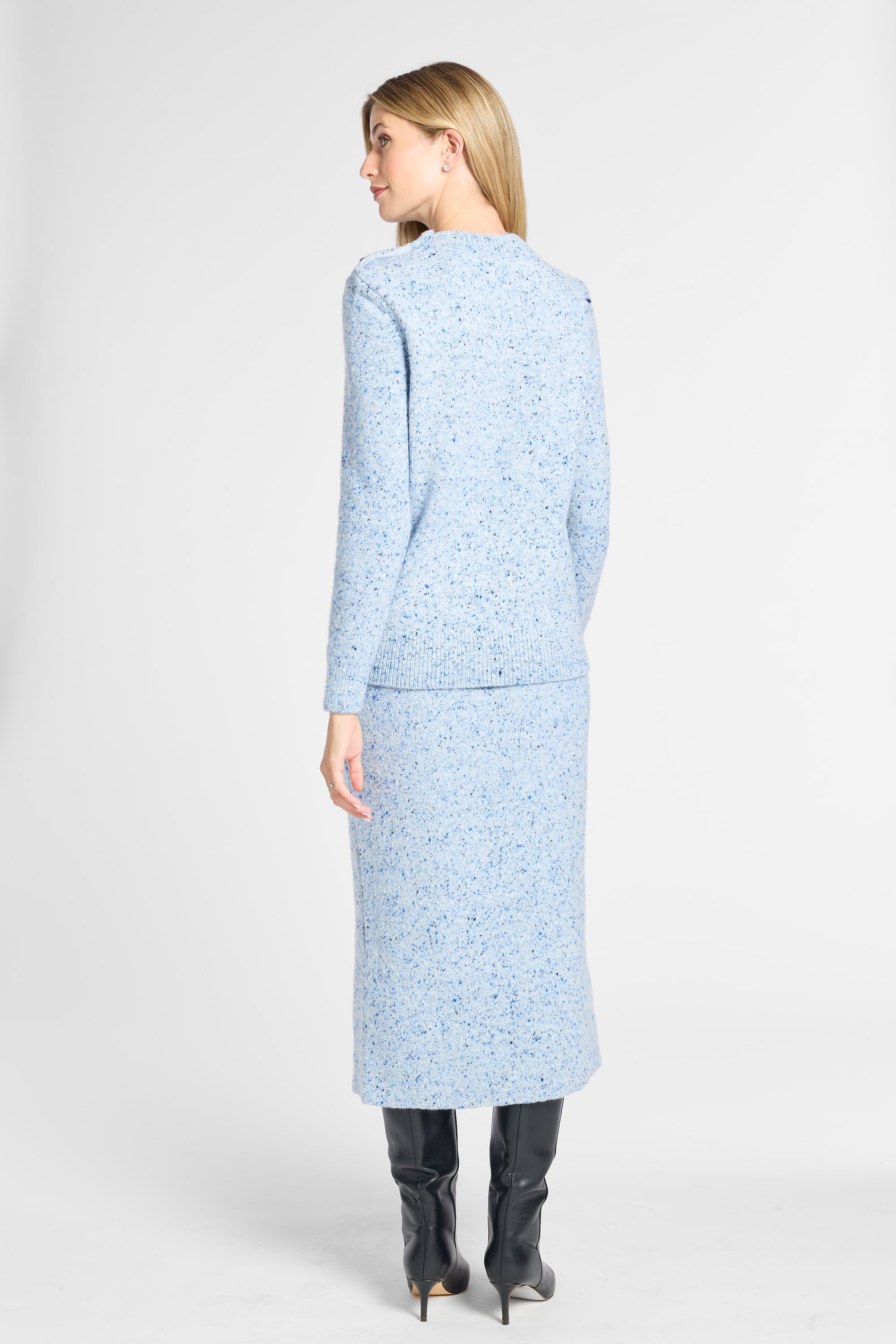 A woman shown from the back wearing a light blue tweed long-sleeve jacket and matching midi skirt set, paired with black knee-high boots, against a plain light gray studio background.