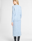 A woman shown from the back wearing a light blue tweed long-sleeve jacket and matching midi skirt set, paired with black knee-high boots, against a plain light gray studio background.