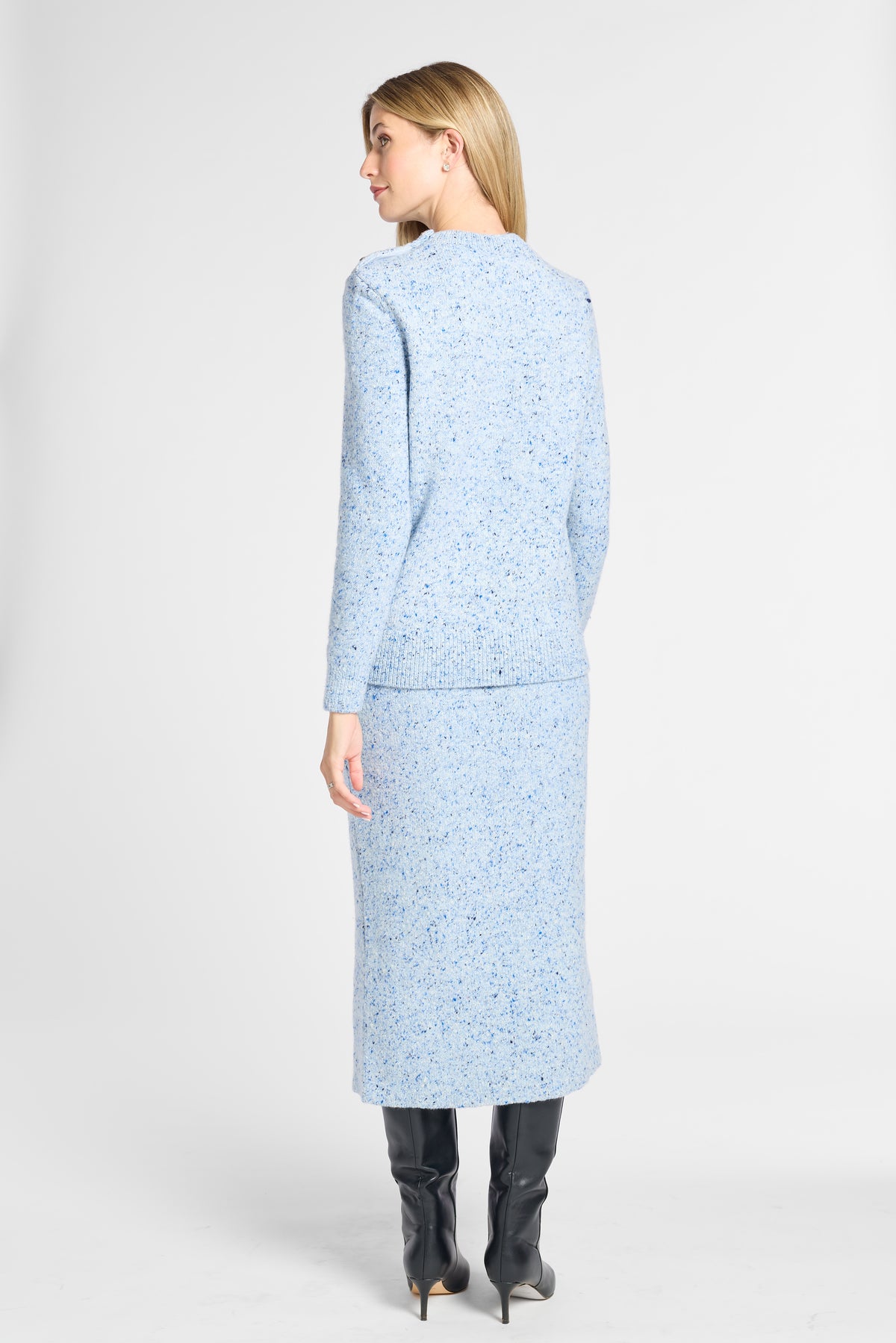 A woman shown from the back wearing a light blue tweed long-sleeve jacket and matching midi skirt set, paired with black knee-high boots, against a plain light gray studio background.