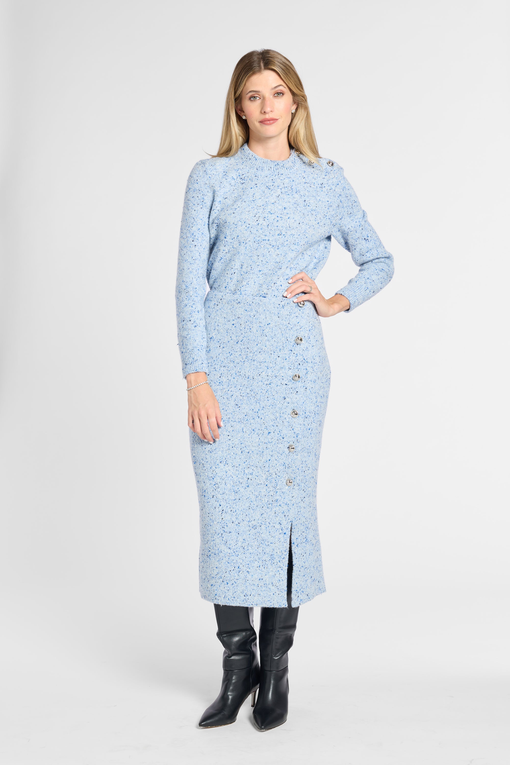 A woman modeling a light blue long-sleeve knit midi dress with a subtle floral pattern, button-front hem, and front slit, paired with black knee-high boots against a light gray studio background.