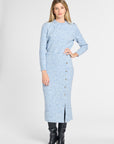 A woman modeling a light blue long-sleeve knit midi dress with a subtle floral pattern, button-front hem, and front slit, paired with black knee-high boots against a light gray studio background.
