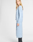 A woman modeling a light blue knit cardigan with a subtle white speckled pattern, paired with black pointed-toe ankle boots, against a plain light gray studio background.
