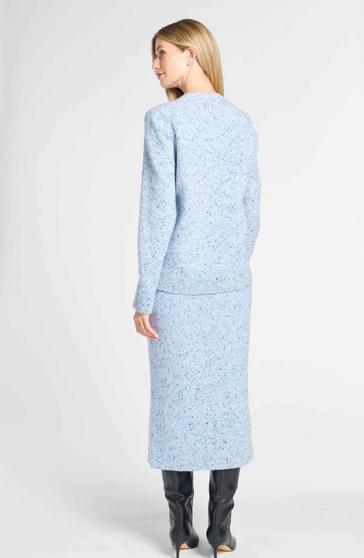A woman shown from the back wearing a light blue tweed long-sleeve top and matching midi skirt, paired with black knee-high boots, against a light gray studio background.