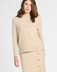A woman modeling a beige knit sweater and matching midi skirt set with brown knee-high boots, photographed against a light gray studio background.