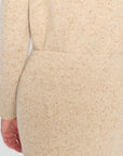 Close-up of a cream-colored knit sweater with subtle tan speckles, showing the ribbed texture and a hand at the side.