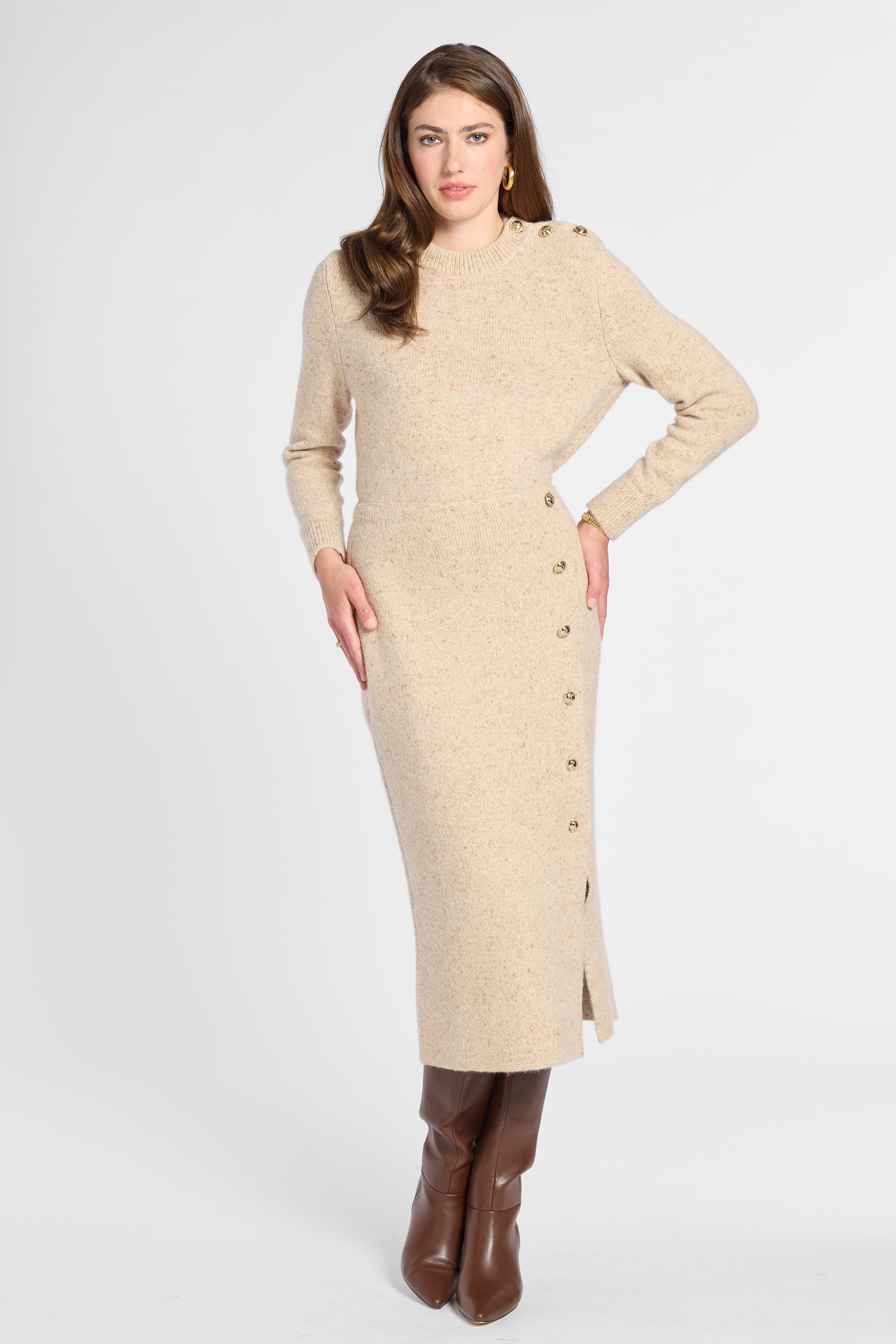 A woman modeling a beige knit long-sleeve midi dress with decorative buttons down the side, paired with brown knee-high boots, against a light gray studio background.