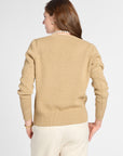 A woman shown from the back wearing a beige knit sweater and cream pants against a light gray studio background.