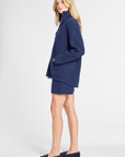A woman modeling a navy blue knit matching set consisting of a mock-neck cardigan and shorts, paired with navy loafers, against a plain light gray studio background.