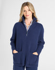 A woman modeling a navy blue knit quarter-zip sweater with matching shorts, featuring a striped inner collar and large front patch pockets, set against a plain light gray studio background.