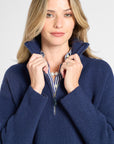 A woman wearing a navy blue ribbed knit half-zip sweater with a striped shirt peeking out at the collar, posing against a light gray background.