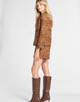 A blonde model is shown from the back wearing a brown tweed jacket and matching mini skirt, paired with brown knee-high boots, against a light gray studio background.