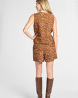 A woman shown from the back wearing a sleeveless, short tweed jumpsuit in a multicolor orange-brown pattern, paired with brown knee-high boots, against a light gray studio background.