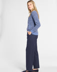 A woman modeling a blue textured knit cardigan sweater and navy wide-leg trousers, standing in profile against a light gray studio background.