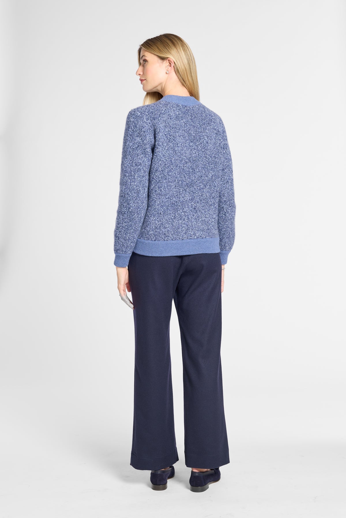 A woman is shown from the back wearing a textured heathered blue sweater and navy wide-leg trousers against a light gray studio background.