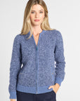 A woman modeling a heathered blue zip-up knit cardigan with ribbed collar, cuffs, and hem, paired with dark navy pants against a light gray studio background.