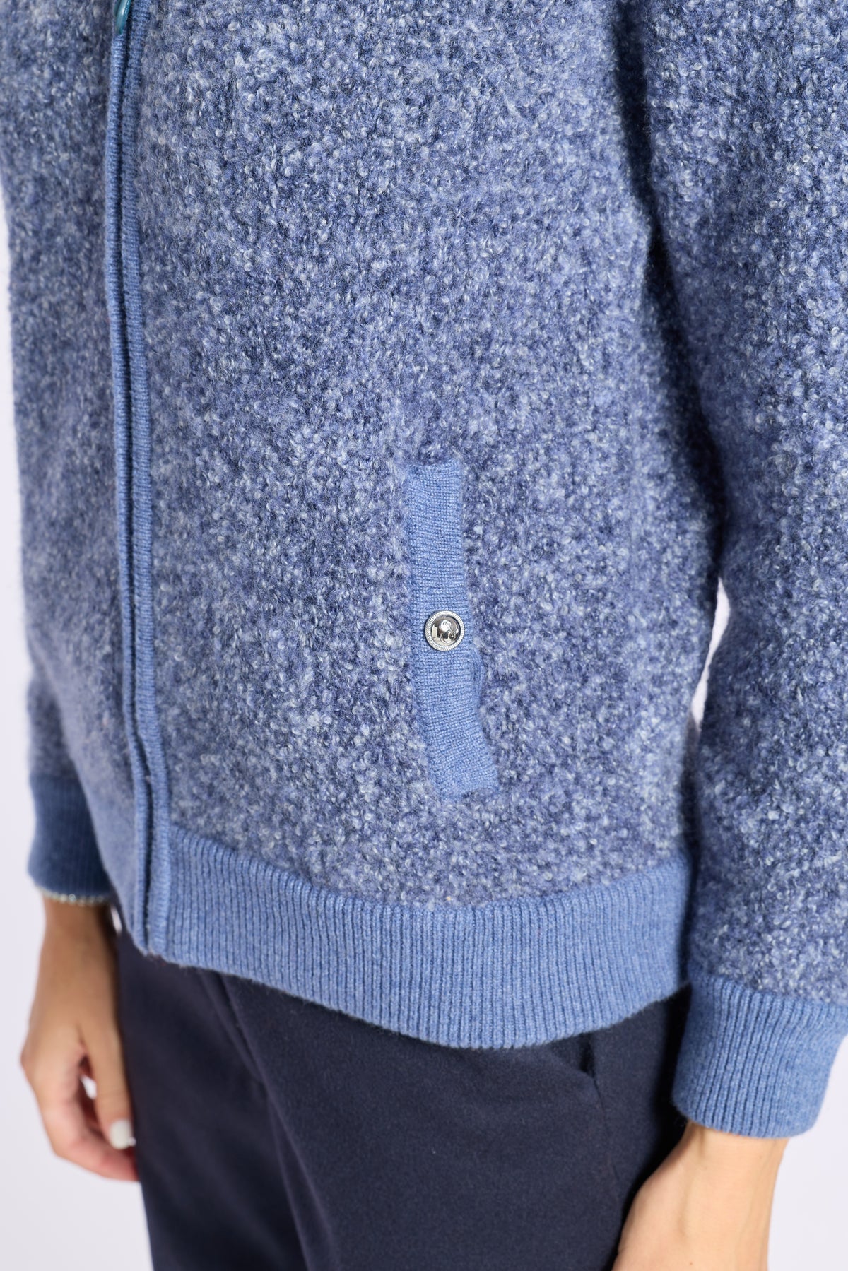 Close-up of a blue heathered knit zip-up cardigan with a ribbed hem and cuffs, featuring a vertical chest pocket with a metal snap button, worn with dark navy pants.