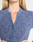 Close-up of a woman wearing a heathered blue zip-front knit sweater with a ribbed collar and cuffs, shown from the shoulders to the hips against a light neutral background.