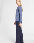 A woman modeling a textured blue knit cardigan sweater paired with navy wide-leg trousers and dark loafers, shown in profile against a plain light gray studio background.