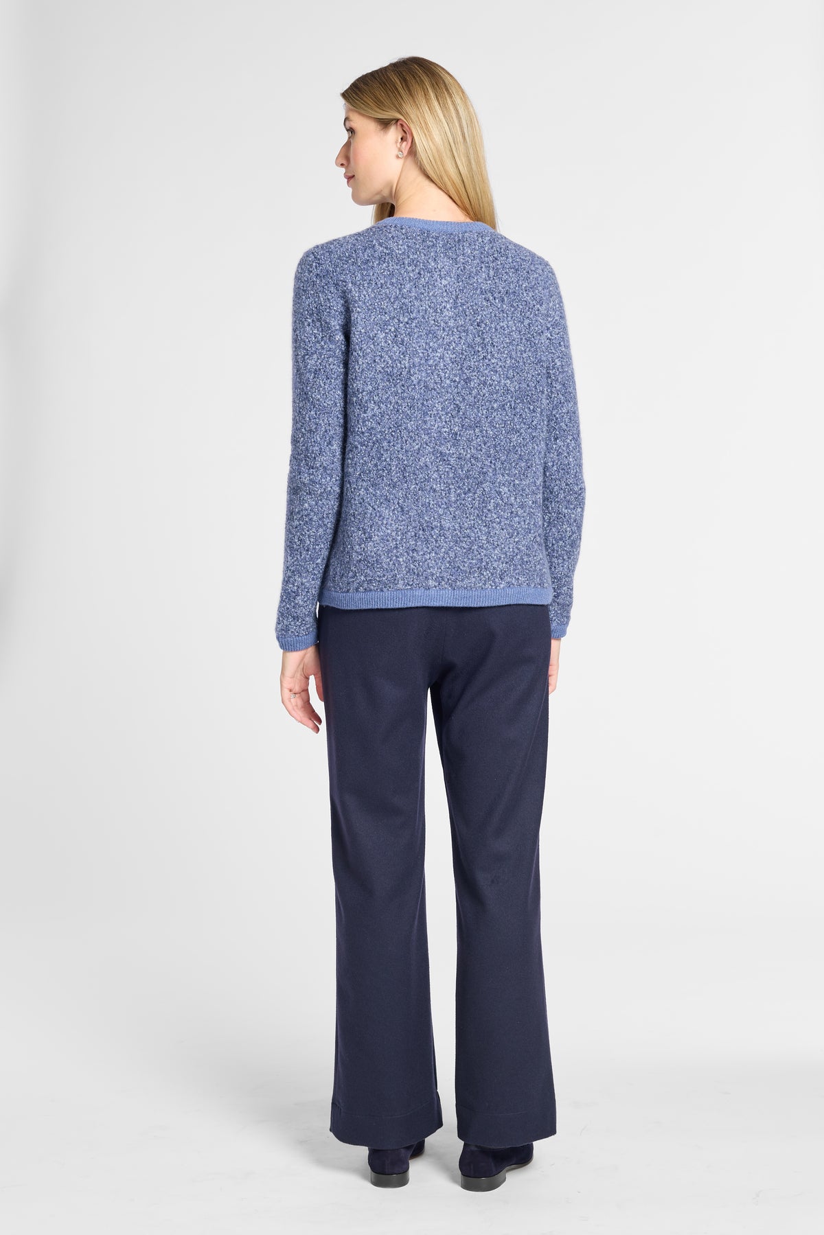 A woman shown from the back wearing a textured heathered blue knit sweater and navy blue wide-leg trousers, photographed against a light gray studio background.