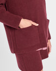 A close-up of a person wearing a ribbed knit quarter zip sweater and matching shorts in a deep burgundy color, with a hand tucked into a pocket and a striped hem detail visible.