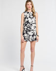 Woman modeling a sleeveless black and white floral blouse on a white backdrop