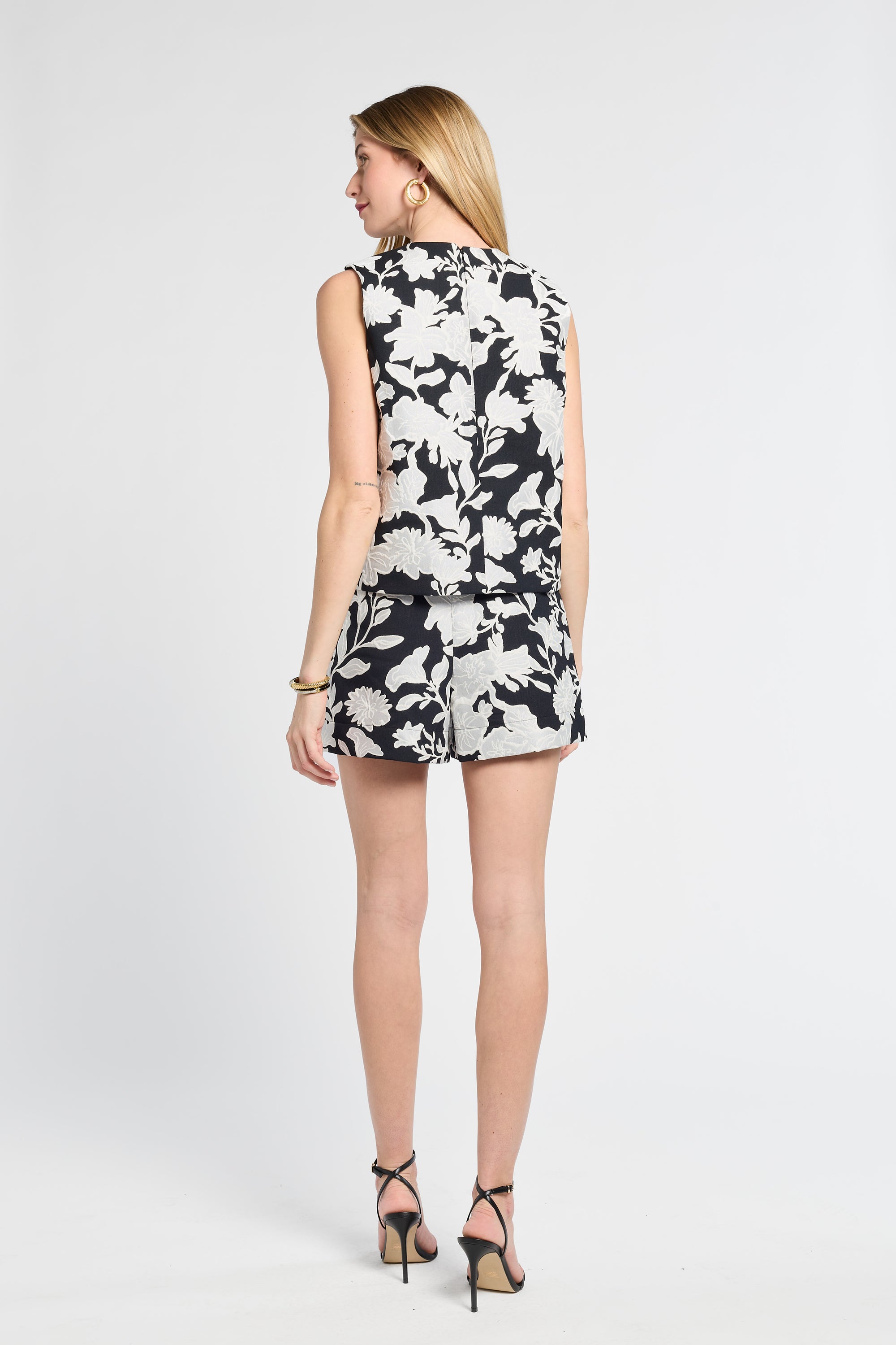 Woman dressed in a sleeveless black and white floral blouse on a white background