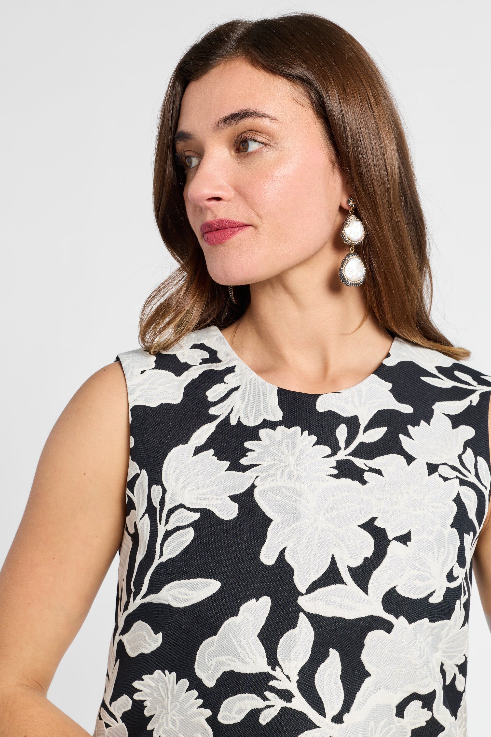 Woman wearing a black and white floral dress with white earrings against a white background