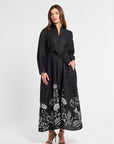 Woman wearing a black maxi dress with floral patterns on a white background