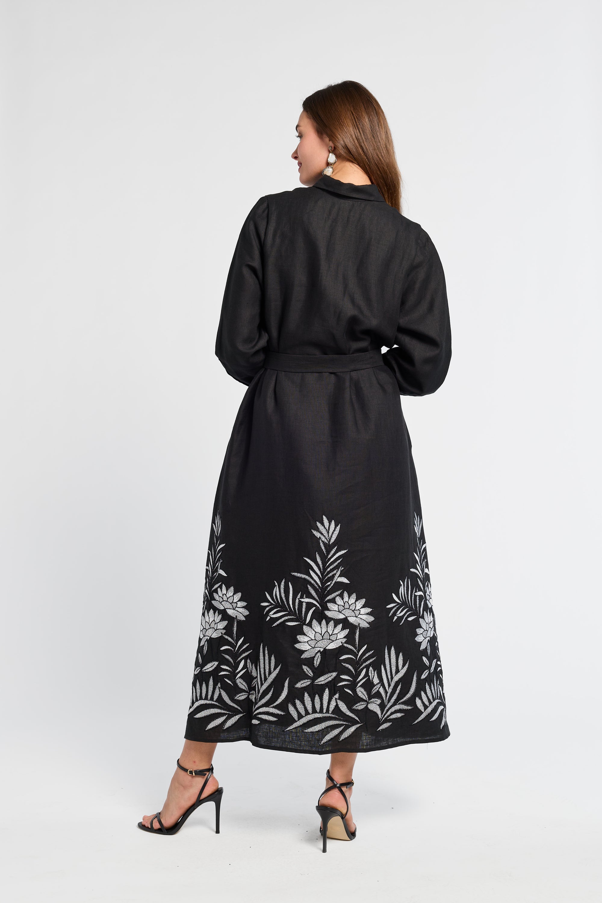 Woman wearing a black dress with floral patterns with black heels on a white background