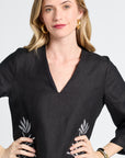 Woman modeling a black dress with floral patterns on a plain background