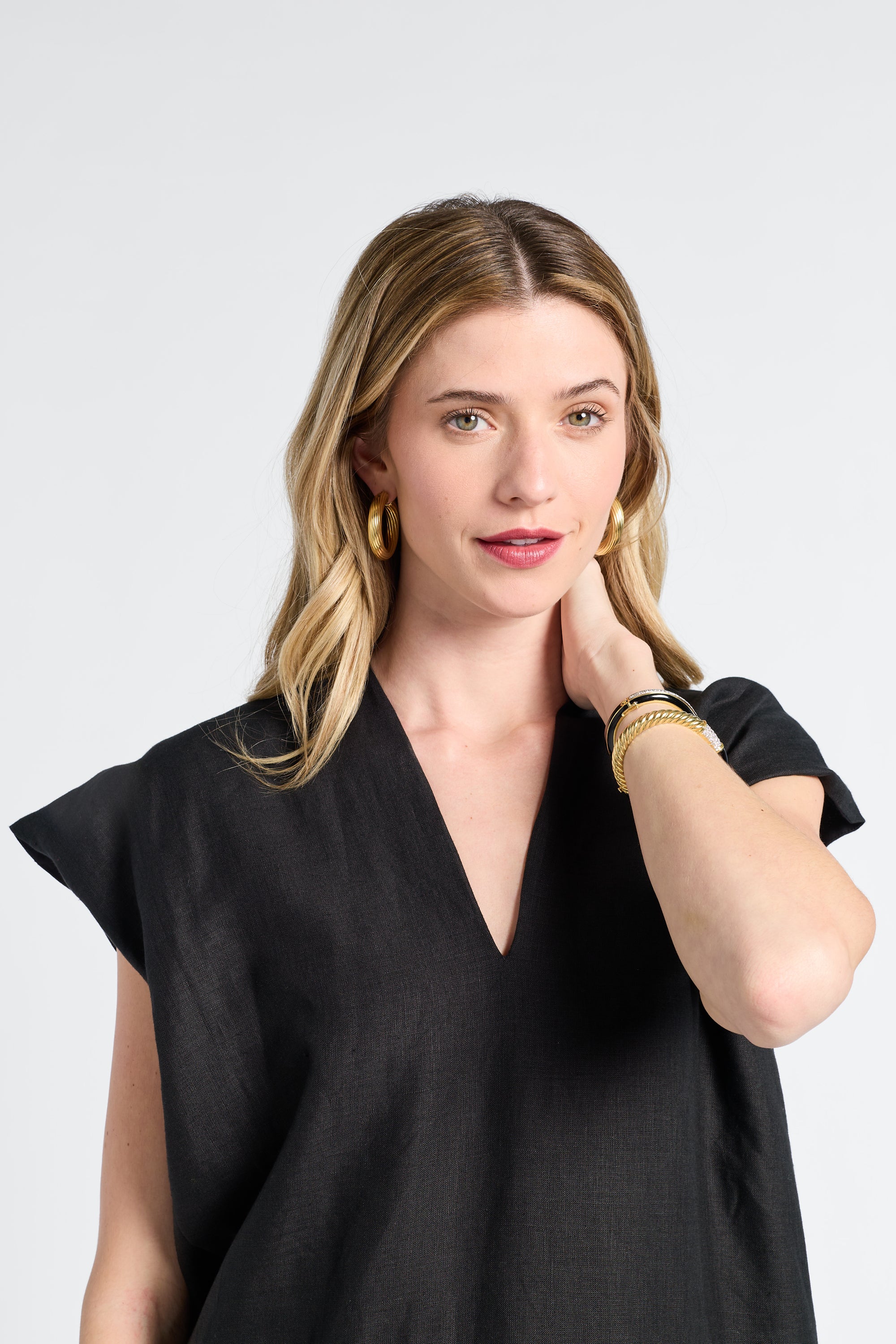 Woman wearing a black caftan with gold jewelry on a white backdrop
