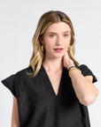 Woman wearing a black caftan with gold jewelry on a white backdrop