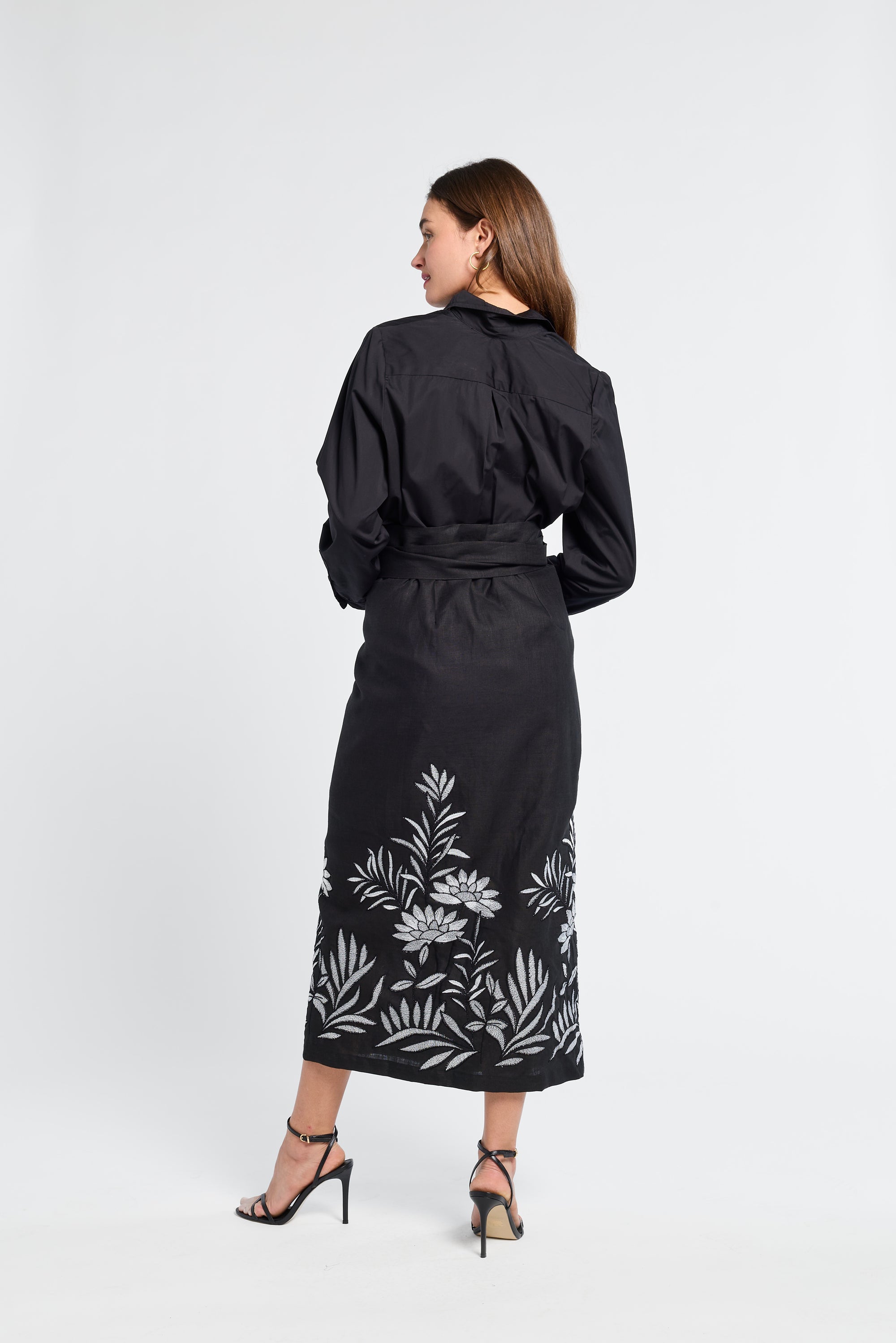Woman wearing a black pareo with white floral patterns and heels on a white background