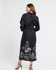 Woman wearing a black pareo with white floral patterns and heels on a white background